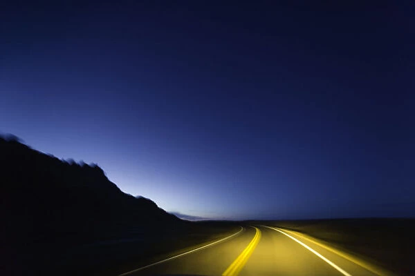 Road past sandstone buttes, lit by headlights, night (blurred motion)