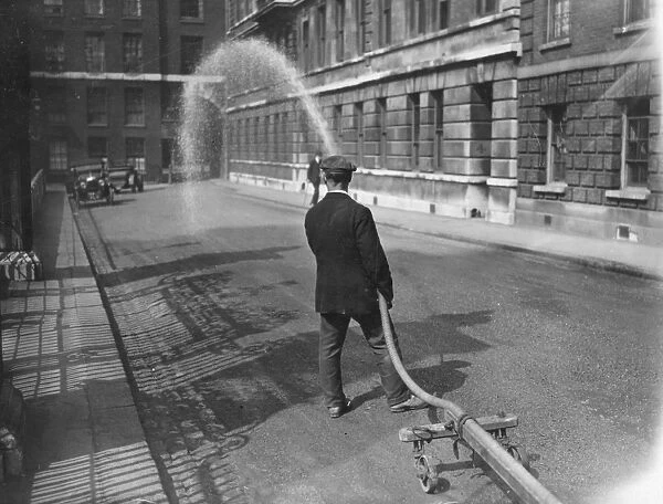 Road Wash. 1925: A roadman spraying down the dust with water in Temple Gardens