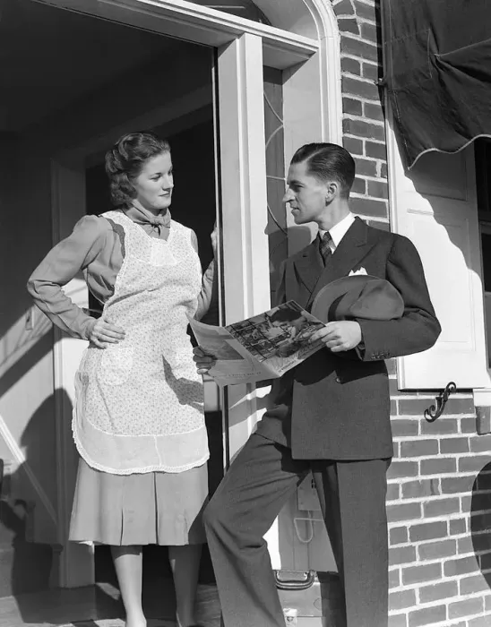 Framed Print : Salesman At Door Of A House Wife Showing Her A Bro
