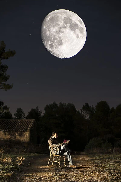 Seated man reading a book in the moonlight