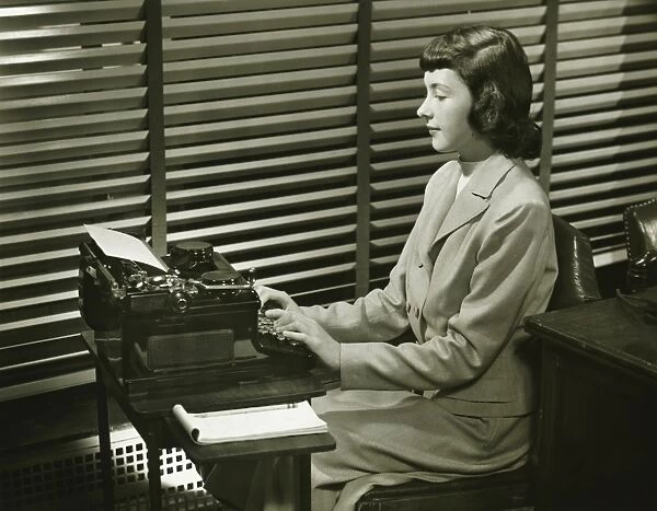 Secretary typing on typewriter in office, (B&W)