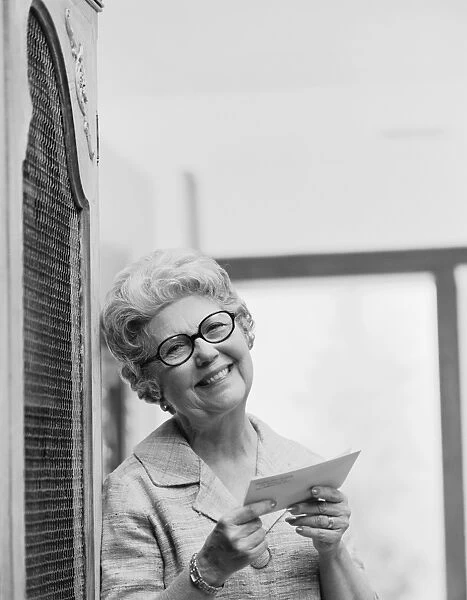 Senior woman holding letter, smiling, portrait