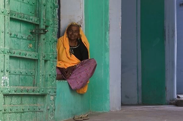 Senior woman sitting in front door of home, smiling, portrait