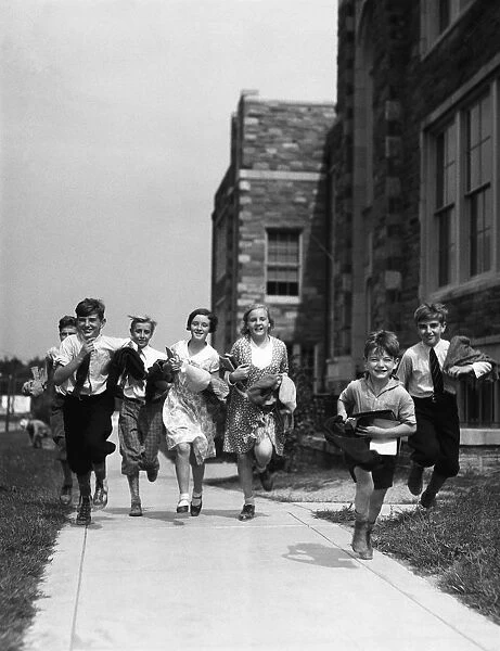 seven children running along pavement, outside schoolhouse