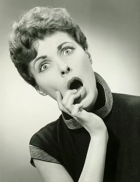 Shocked woman with fingers on lips in studio, (B&W), portrait