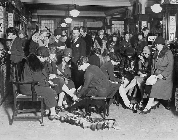 Shoe Sale. Customers trying on shoes in a crowded shop during a sale, 1929