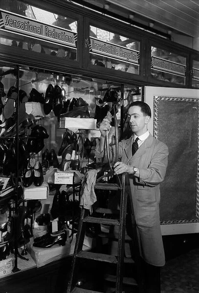 Shoe Sale. circa 1930: An assistant dressing a window for a shoe sale