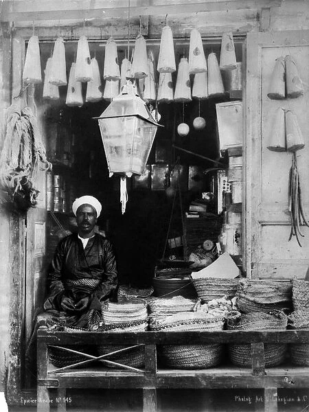 Shopfront. circa 1900: An African shopkeeper selling lanterns and household goods