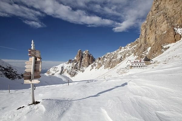 Signpost, Tierser Alplhutte mountain cabin and Rosszahne peaks in winter, Seiser Alm alp, Province of South Tyrol, Italy