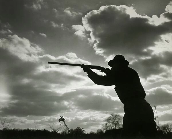 Silhouette of man aiming shotgun outdoors