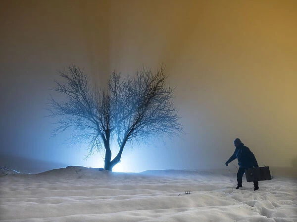 Silhouette of a person walking with a suitcase, for a covered way of snow and fog during the night