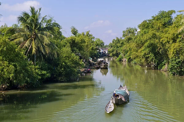 Small wooden motorboat passing through a water channel surrounded by tropical vegetation, Hue, Vietnam, Asia