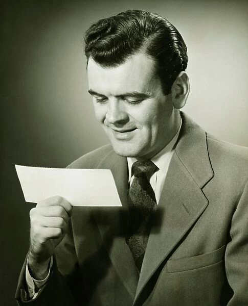 Smiling businessman looking at bank check, (B&W), portrait