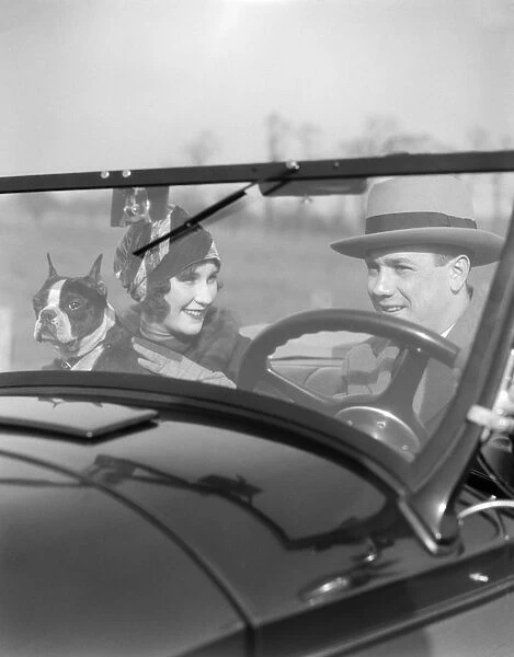 Smiling Couple With Dog Boston Terrier In Front Seat Of Convertible View Through The Windshield Into The Car Man At Steering Wheel Fashion Hats