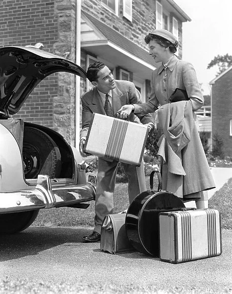 Smiling couple load suitcases into trunk of sedan