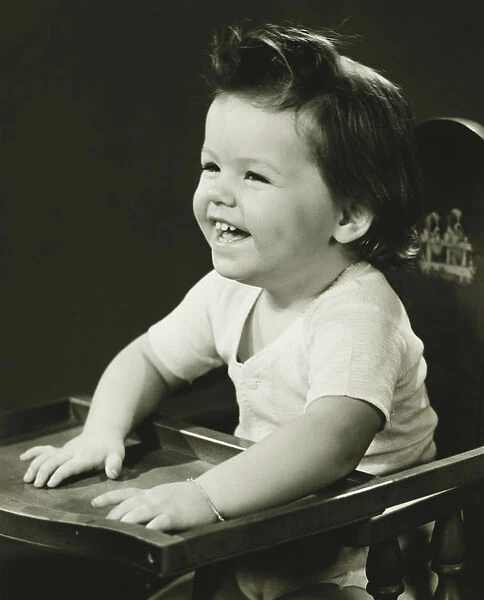 Smiling girl (2-3) sitting in high chair, (B&W)