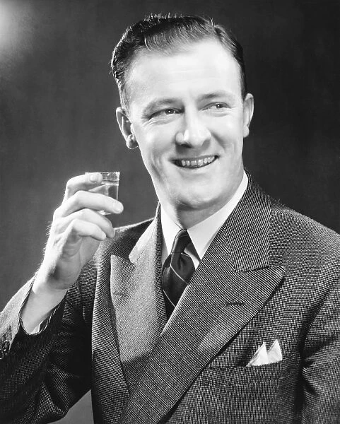 Smiling man holding up short glass with drink, (B&W), close-up