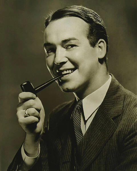 Smiling man with pipe in mouth posing in studio, (B&W), close-up, portrait