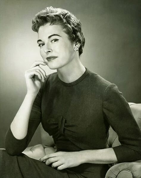 Smiling woman sitting in armchair in studio, (B&W), portrait