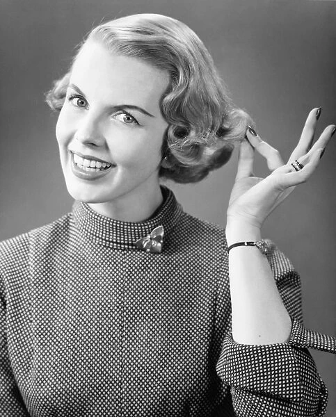 Smiling woman touching hair posing in studio, (B&W), portrait, close-up
