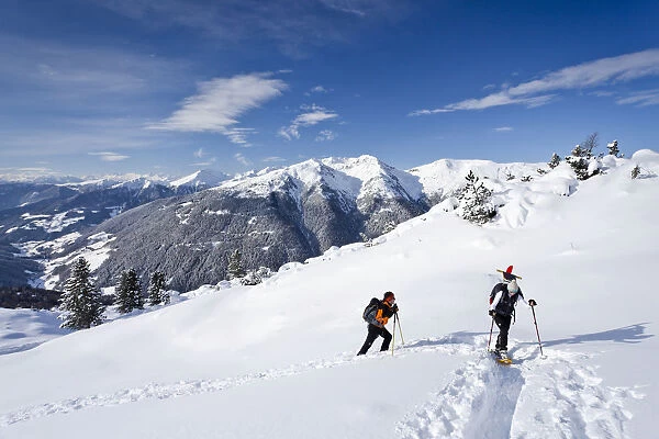 Snowshoe walkers during the ascent of the Mt Morgenrast summit from Unterreinswald, Sartntal valley and its mountains at back, South Tyrol, Italy, Europe