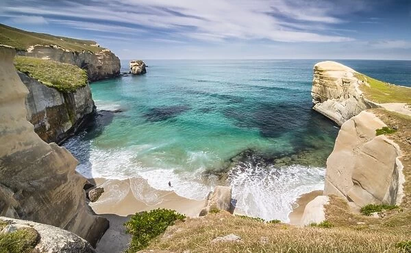 Solitary person on the rocky cliffs of the Pacific coast in the distance, bay at Tunnel Beach, Dunedin, Otago Region, South Island, New Zealand