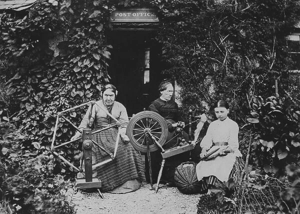Spinners. circa 1885: Women spinning and carding wool outside the local
