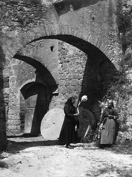 Spinners. circa 1910: Two old women spinning by hand under the Archi del