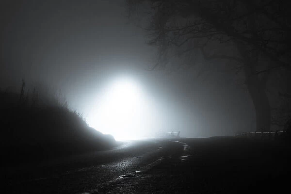 A spooky, eerie country road passing through a hill. With a light in the distance