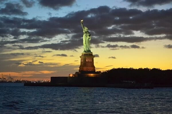 Statue of Liberty illuminated at sunset with dramatic sky, New York City, USA