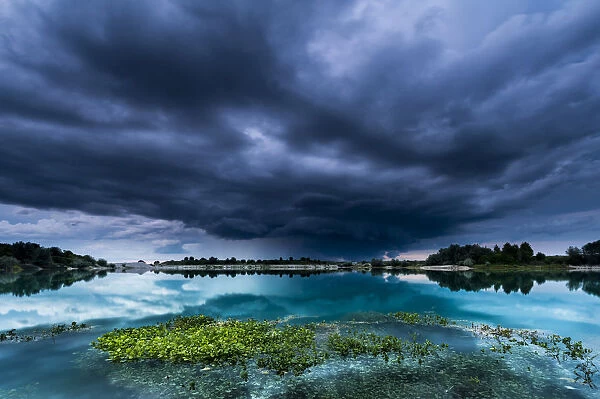 Storm clouds over a quarry lake with water plants, near Mindelheim, Unterallgau, Allgau, Bavaria, Germany