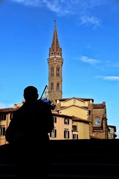 Street musician plays a violin in front of Badia Fiorentina bell-tower in Florence, Italy