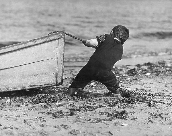Stuck In The Mud; young boy in a swimsuit stands ankle-deep in mud on beach using