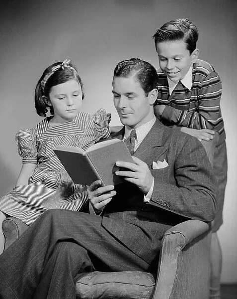 Studio shot of father with two children (10-11) reading book