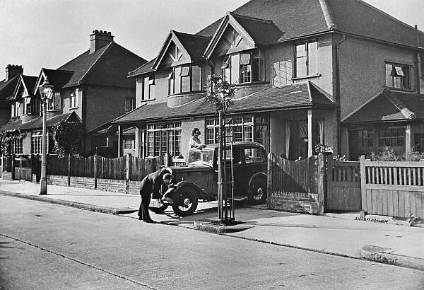 Suburbia. A couple washing their car outside their house in the suburbs, circa 1930