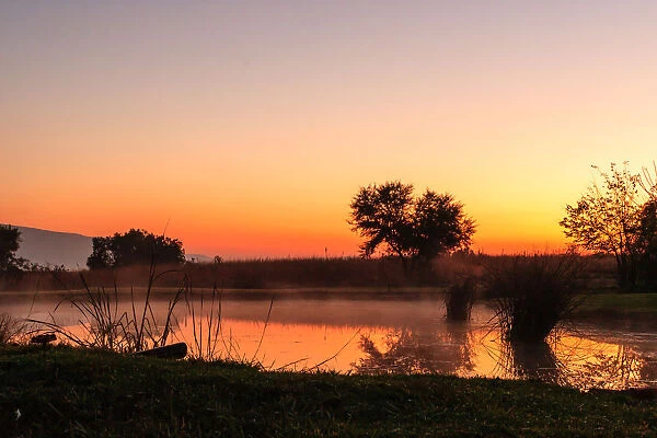 The sun rises over a small dam in the high veld winter landscape near Hartebeespoort, South Africa