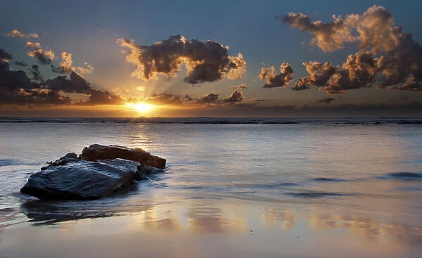 Sunrise landscape of ocean with waves clouds and rocks on beach