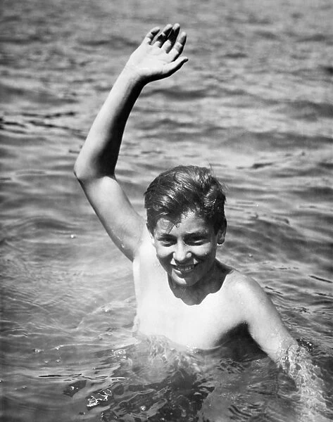 Teenage boy (16-17) standing deep in water, waving, (B&W), portrait