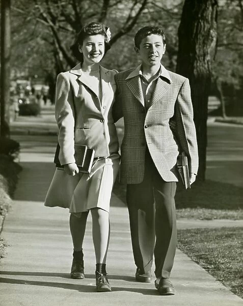 Teenage couple (16-17) walking on park, (B&W)