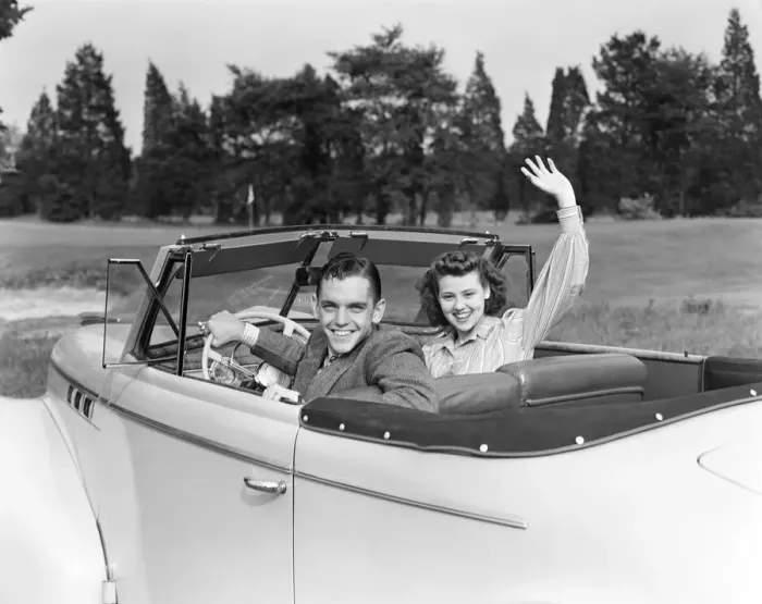 Framed Print : Teenage couple in convertible car smile and wave to viewer