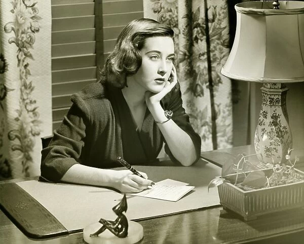 Thoughtful woman writing letter at desk, (B&W)