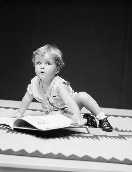Toddler boy with open book, looking away