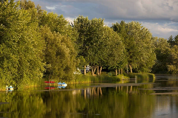 Trees and boats on Yamaska River in evening light with threatening clouds, Waterloo, Eastern Townships, Quebec Province, Canada