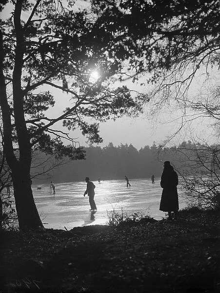 Twilight. 8th December 1933: A solitary figure comtemplates skaters on a frozen lake