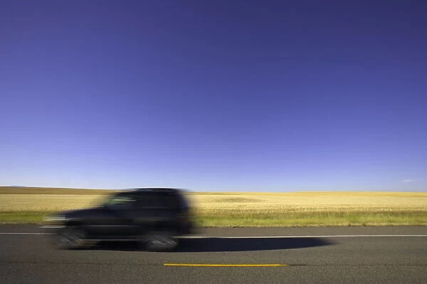 USA, Montana, SUV on highway beside wheatfield (blurred motion)