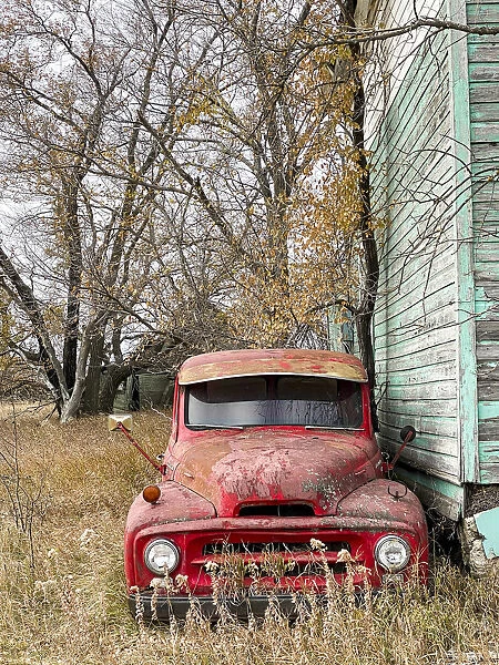 A vintage red pick-up truck parked beside an abandoned house