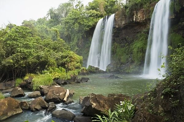 Three waterfalls in tropical landscape with flowers in foreground