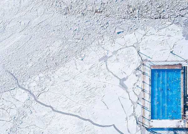 Wintery top-down aerial view of a heated swimming pool next to frozen Baltic sea
