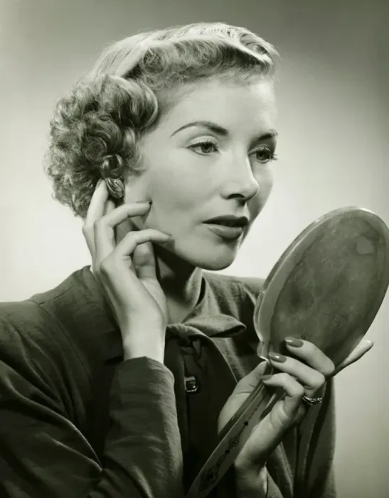 Framed Print : Woman adjusting earring, holding hand mirror, (B&W), portrait Framed Print : Woman adjusting earring, holding hand mirror, (B&W), portrait