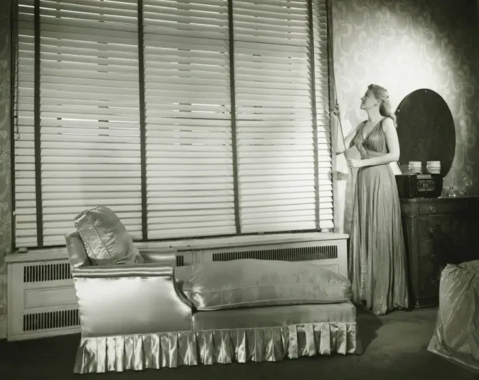 Framed Print : Woman adjusting window blind in living room, (B&W) Framed Print : Woman adjusting window blind in living room, (B&W)